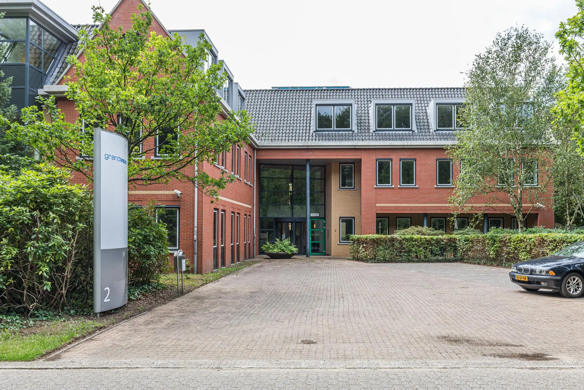 Bakstenen kantoorpand aan de Laan Blussé van Oud-Alblas 2 met entree, parkeerplaats en duidelijke bewegwijzering van GrandVision.